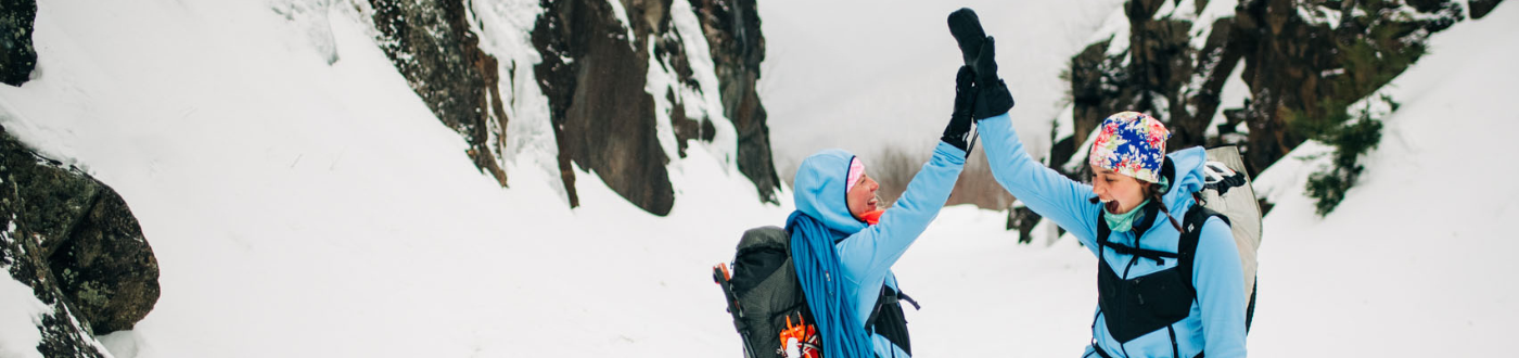 Two female hikers high-5 while both wearing Women's Washington Outer Layers in 'Classic Blue.'