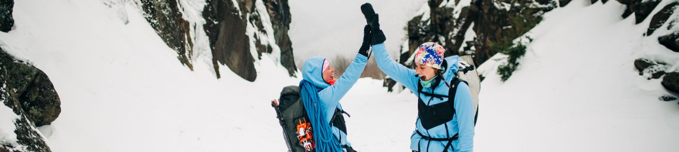 Two female hikers high-5 while wearing Washington Outer Layers in 'Classic Blue.'